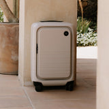 Monos Carry - On Pro Plus Luggage (23"), Hardside Spinner Suitcase with TSA Lock & Front Pocket, Airline Approved, Desert Taupe, Beige